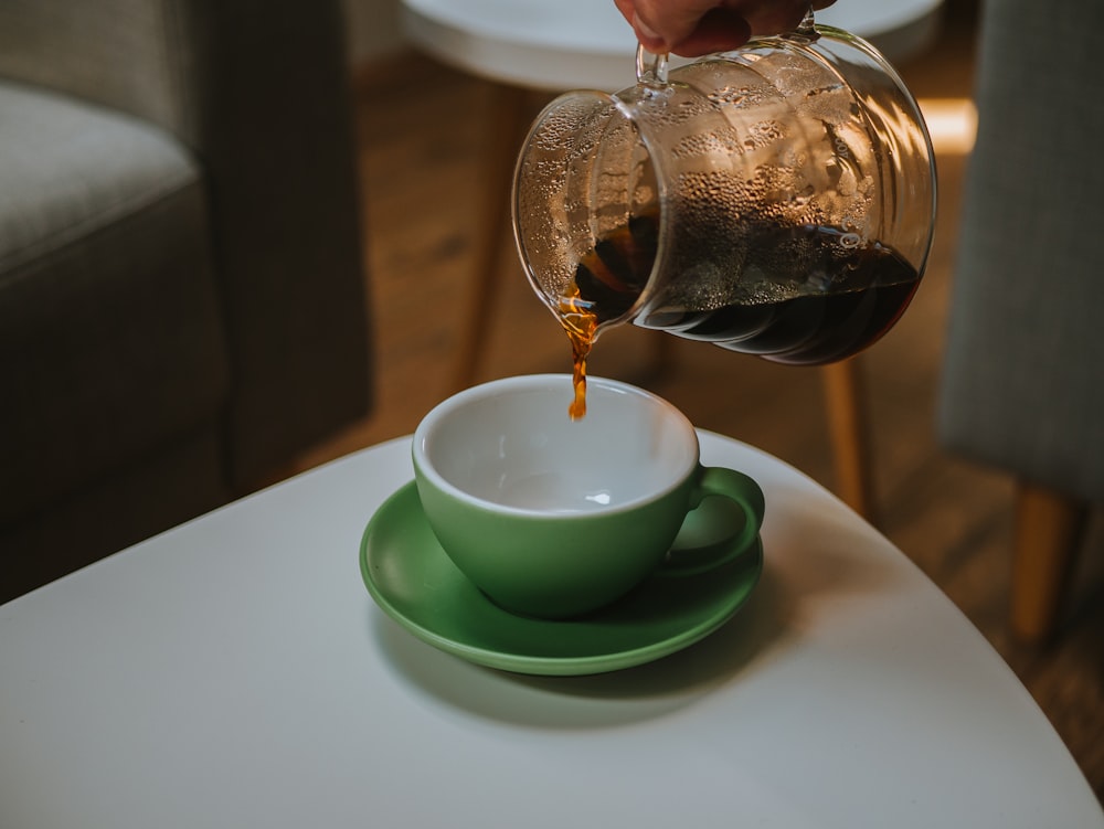 taza de té de cerámica verde y blanca sobre mesa blanca