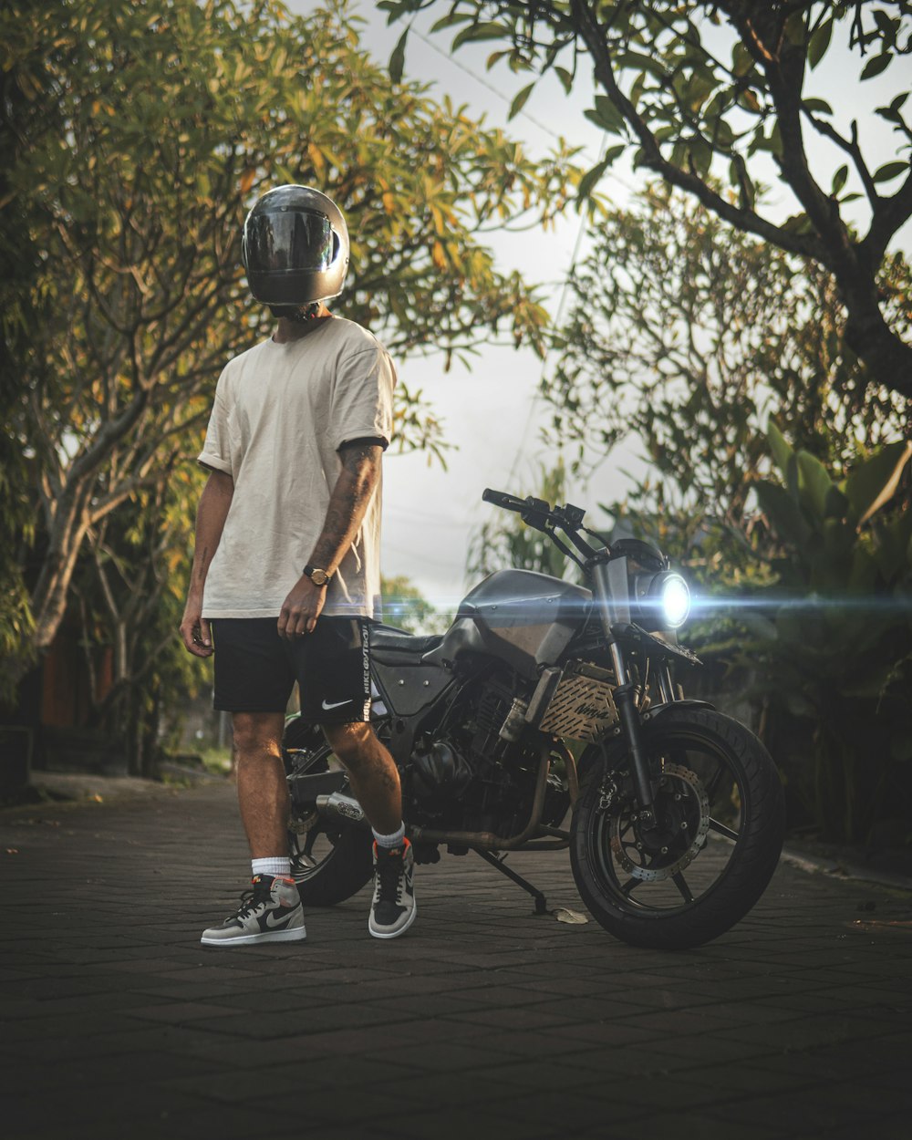 man in white crew neck t-shirt and black shorts standing beside black motorcycle during daytime