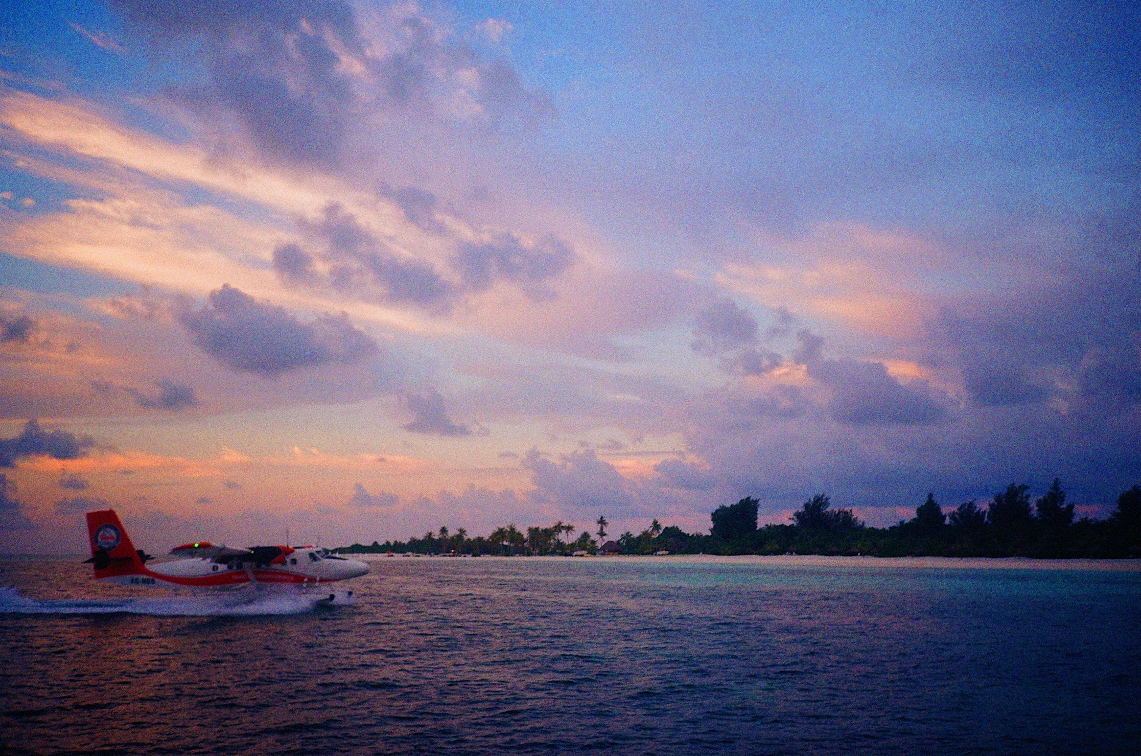 A seaplane skimming across a lagoon at dusk, with a palm-covered island beyond, the Maldives
