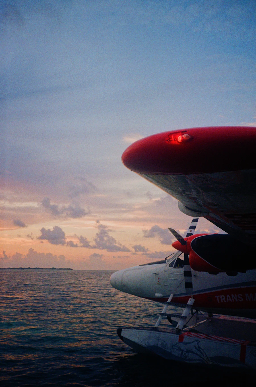 Seaplane flying low over the ocean as the sun sets behind the horizon