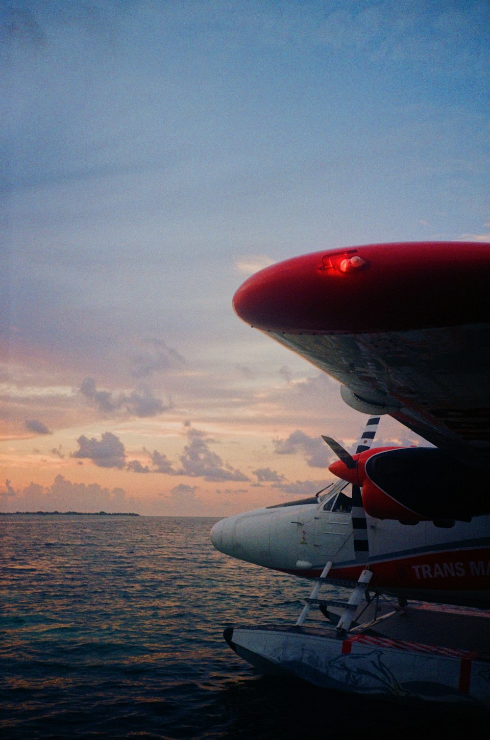 white and red airplane flying over the sea during sunset