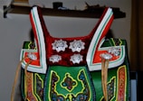 An intricately decorated traditional saddle features vibrant colors, with detailed patterns and ornate silver embellishments. The combination of leather and metal elements creates an exquisite and cultural appearance.