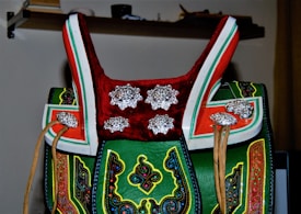 An intricately decorated traditional saddle features vibrant colors, with detailed patterns and ornate silver embellishments. The combination of leather and metal elements creates an exquisite and cultural appearance.