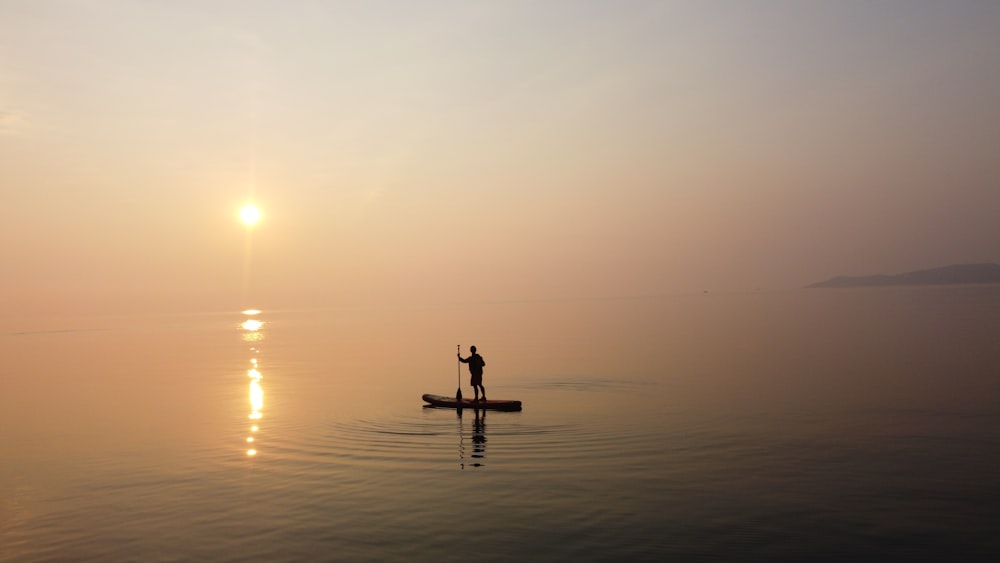 silhouette of person standing on sea shore during sunset