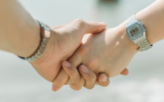 close up of two white people's hands holding each other, they are both wearing silver watches