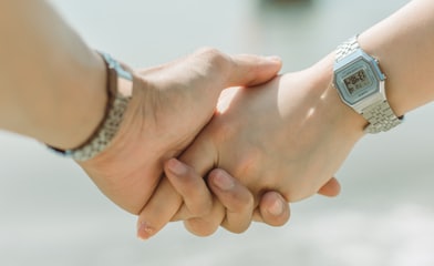 close up of two white people's hands holding each other, they are both wearing silver watches