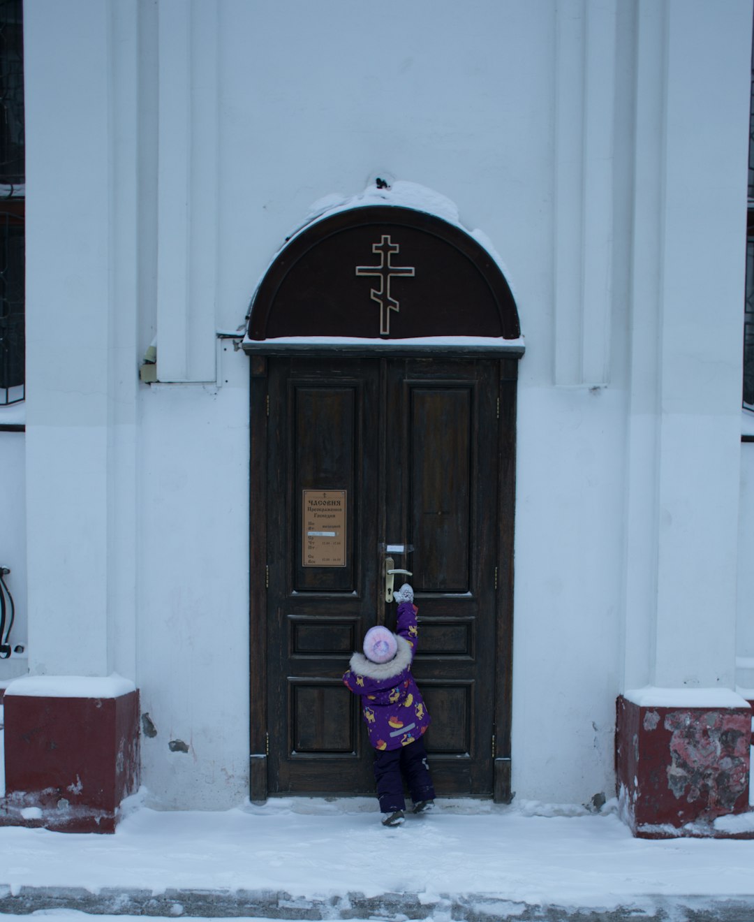 girl in purple jacket standing beside brown wooden door