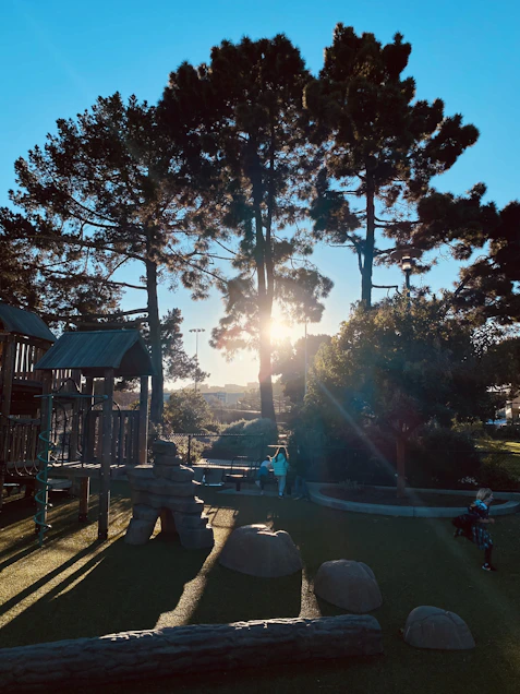 A cheerful sun shining over a playful preschool playground with kids laughing.