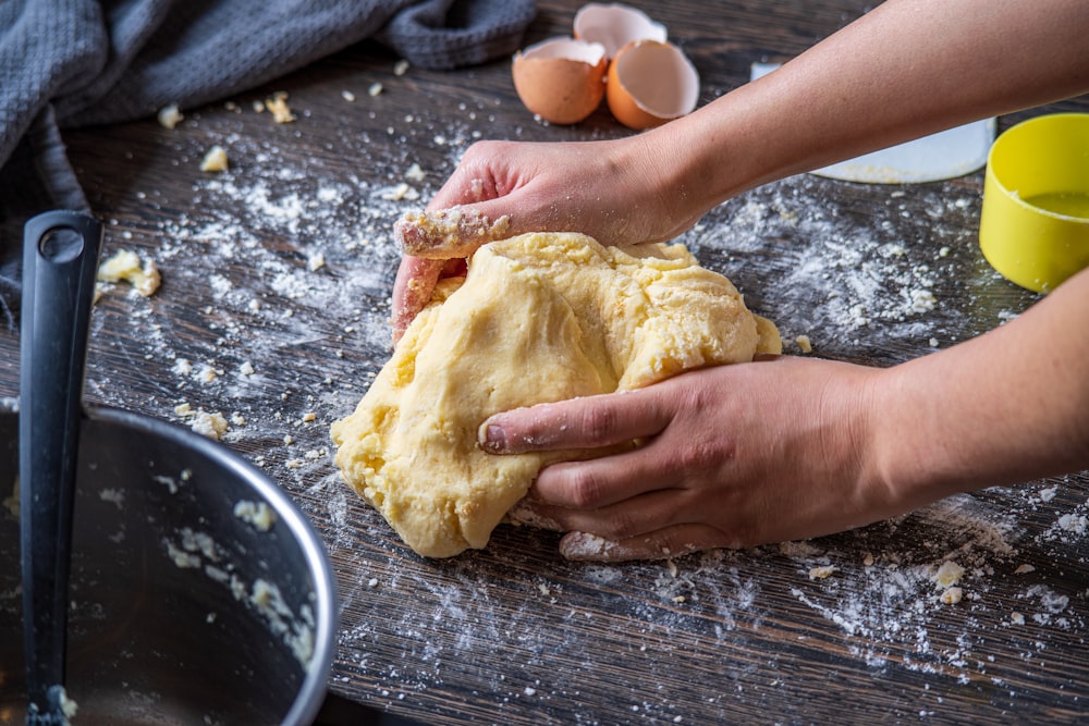 Persona che tiene il pane sul tavolo di legno marrone