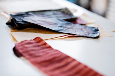 Several pieces of textured fabric and paper are arranged on a flat surface. The fabrics vary in color and texture, with some appearing crumpled or wrinkled. The focus is on the mix of materials suggesting a creative or artistic setting.
