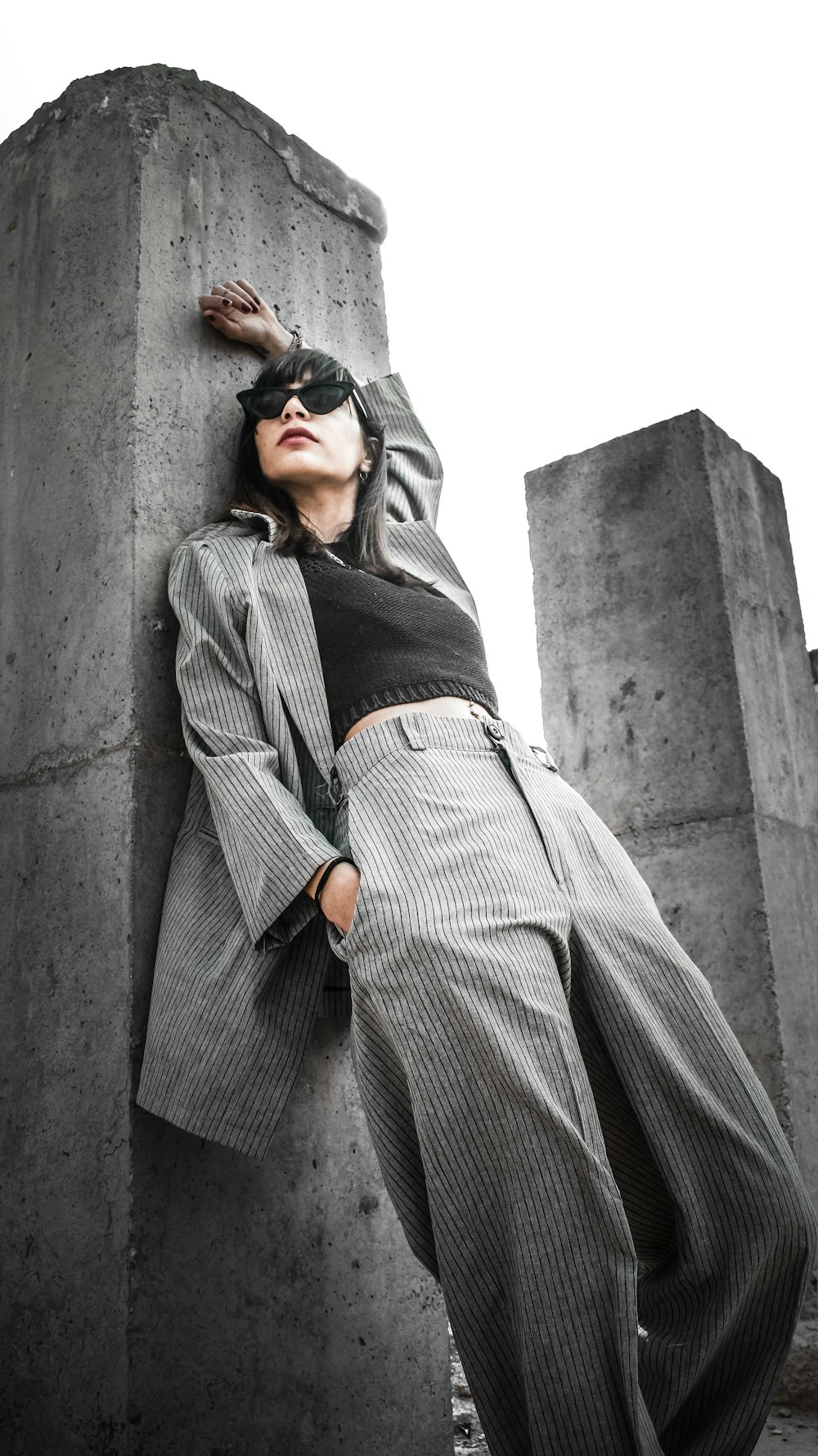 man in black and white pinstripe dress shirt and black sunglasses leaning on gray concrete wall