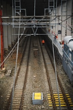 Workers in bright orange safety gear installing physical barriers along a German railway track with concrete sleepers and overhead lines.