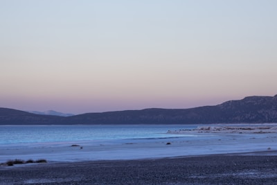 A peaceful lakeside view with soft ripples reflecting a pastel sunrise sky.