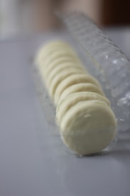 A row of round white chocolate-covered cookies placed in a clear plastic tray. The cookies are aligned neatly and the focus is on the foreground, creating a softly blurred background.