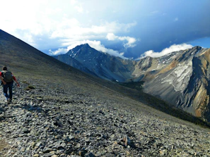 A traveler wearing a durable backpack while hiking on a rocky trail with mountains in the background.