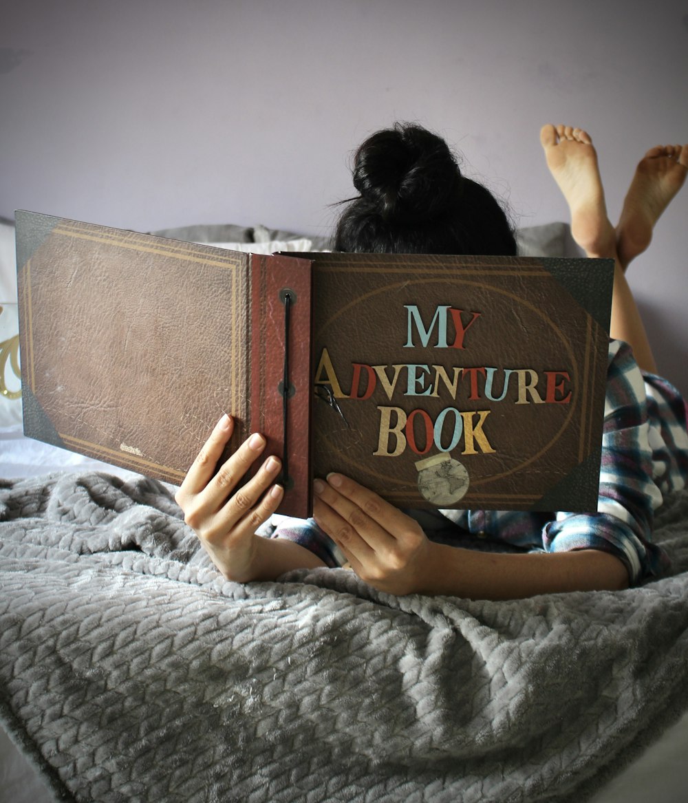 person holding brown book lying on bed