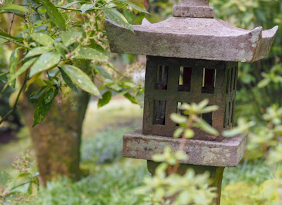 Close-up of a weathered stone lantern nestled among ferns and fallen leaves.