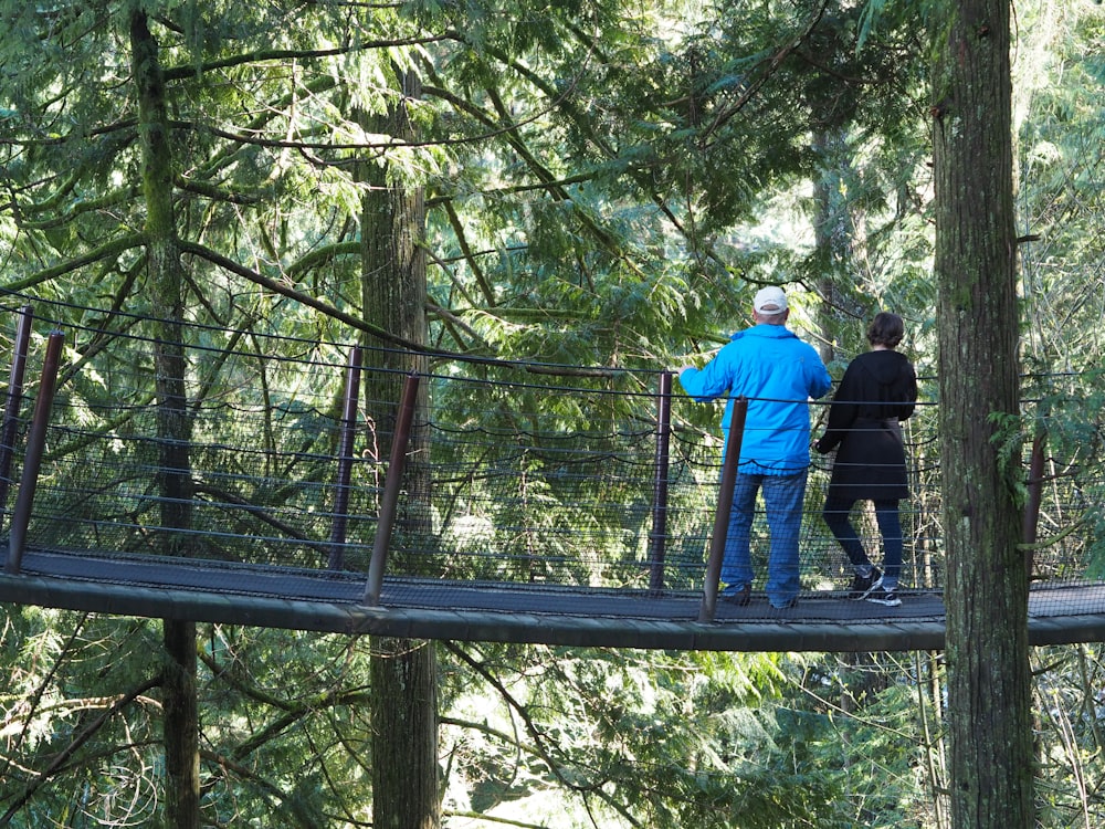 man in blue jacket and black pants standing on brown wooden bridge