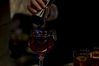 person pouring red liquid on clear wine glass