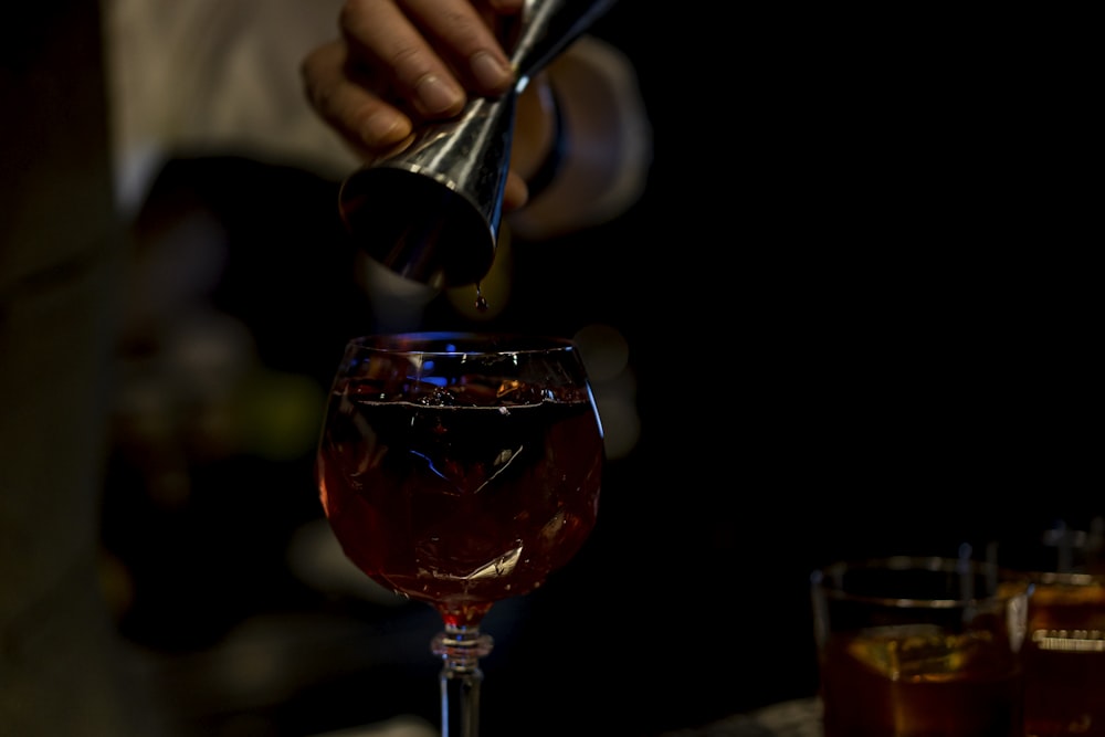 person pouring red liquid on clear wine glass