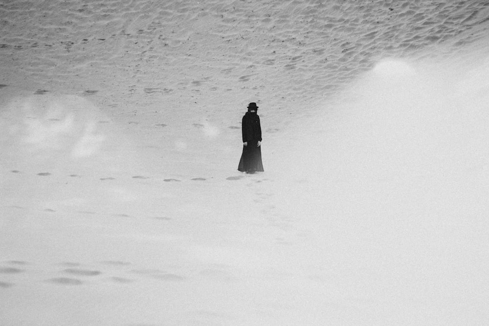 personne en manteau noir marchant sur un champ enneigé pendant la journée
