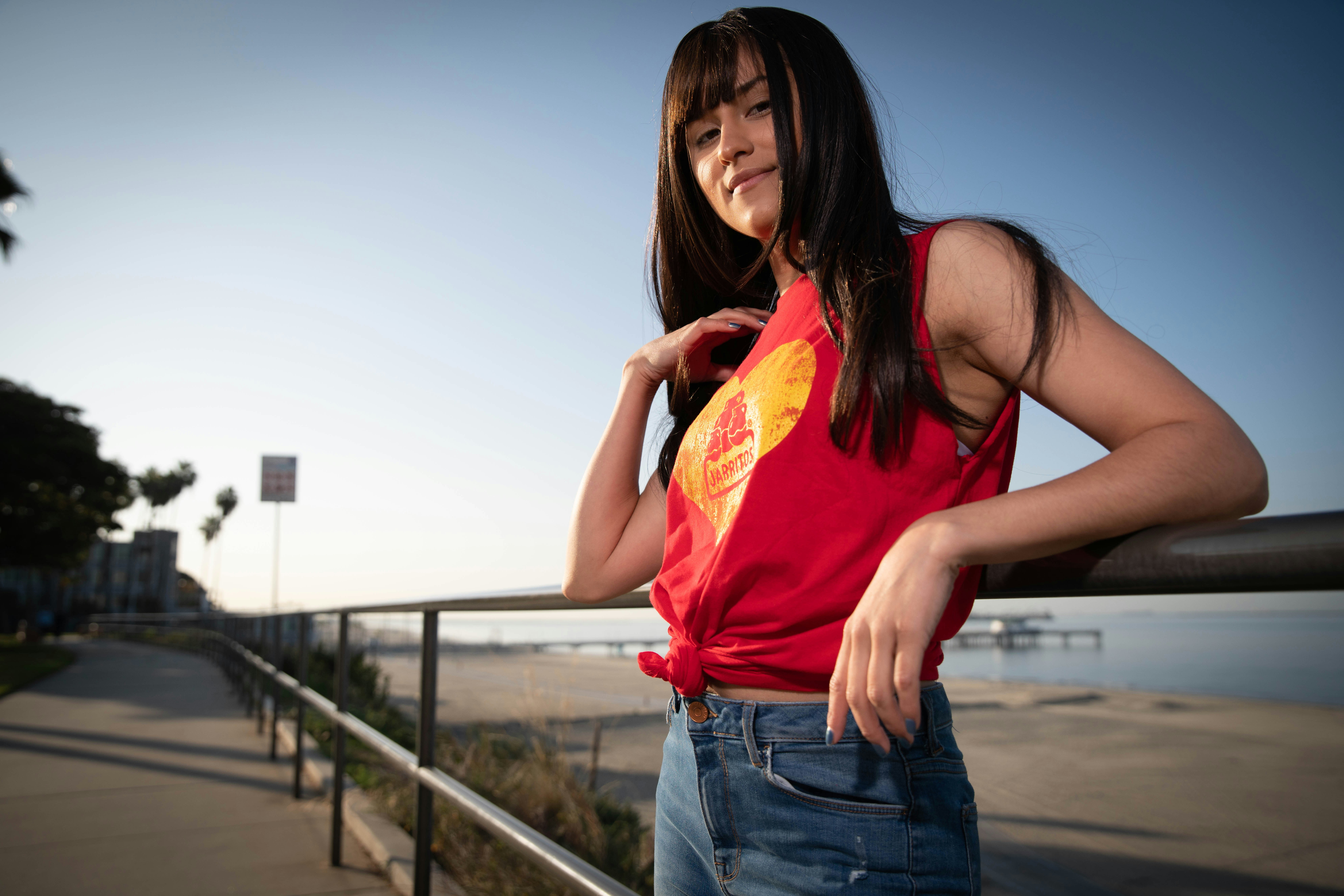 Wanita dengan tank top merah dan celana pendek denim biru memegang paket plastik kuning