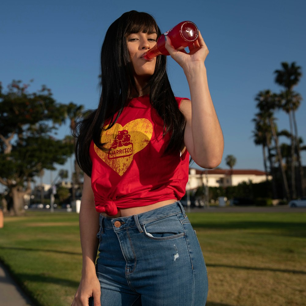 woman in red t-shirt and blue denim jeans holding red ceramic mug