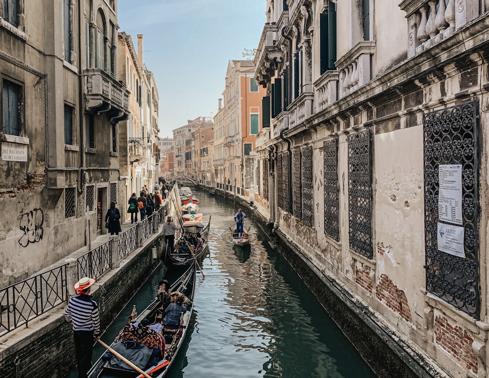 people riding on boat on river between concrete buildings during daytime