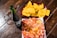 A glass bottle of soda sits on a wooden table beside a plate of nachos with a cheese dip topped with lime, chili powder, and drizzled sauce. A separate plate holds crispy tortilla chips.