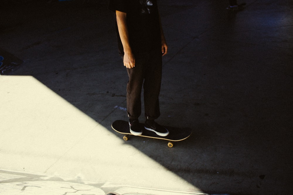 person in black pants and black shoes standing on black skateboard