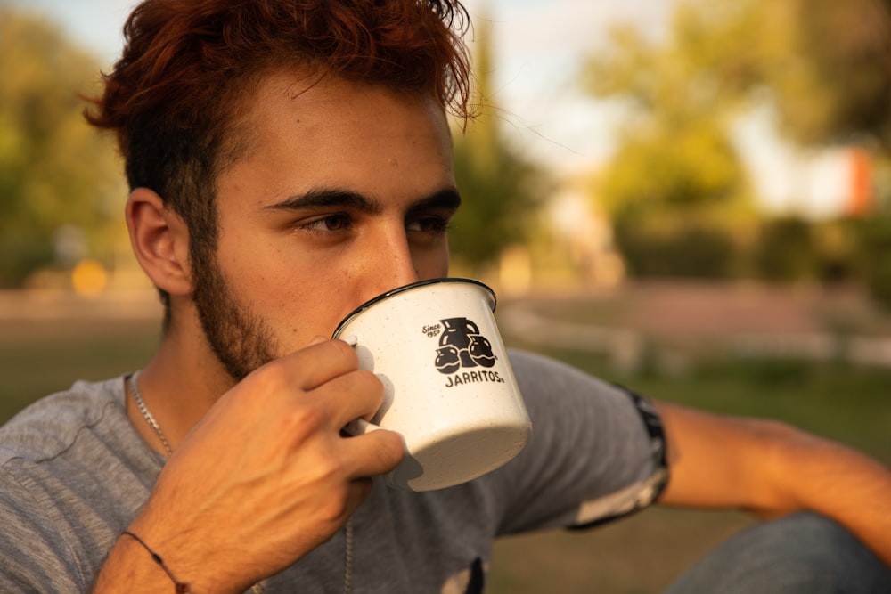 man in gray shirt drinking from white ceramic mug