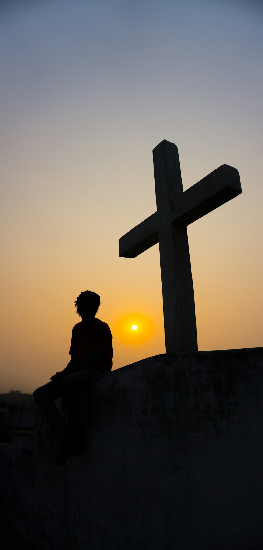 silhouette of man sitting on the edge of a cross during sunset