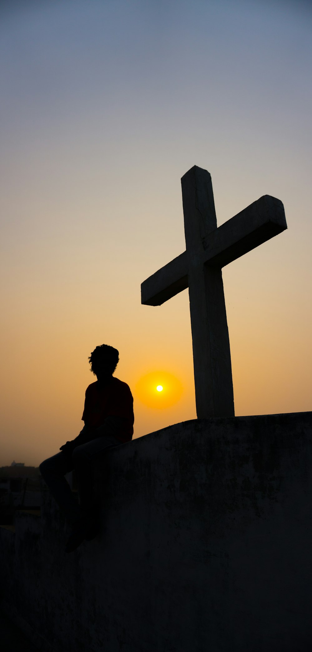 silhueta do homem sentado à beira de uma cruz durante o pôr do sol