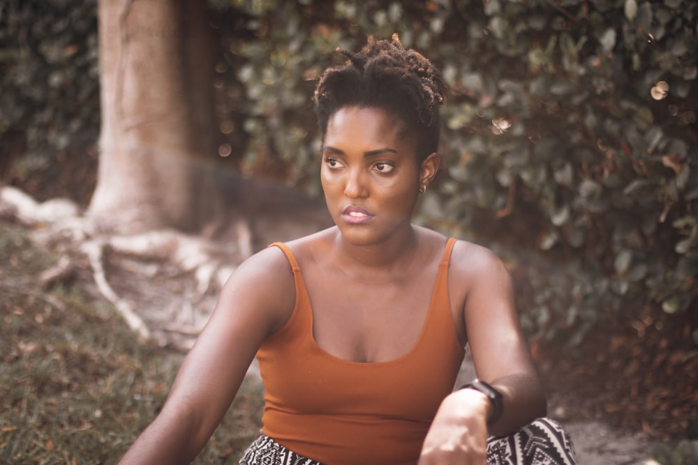 woman in orange tank top and black and white pants sitting on ground