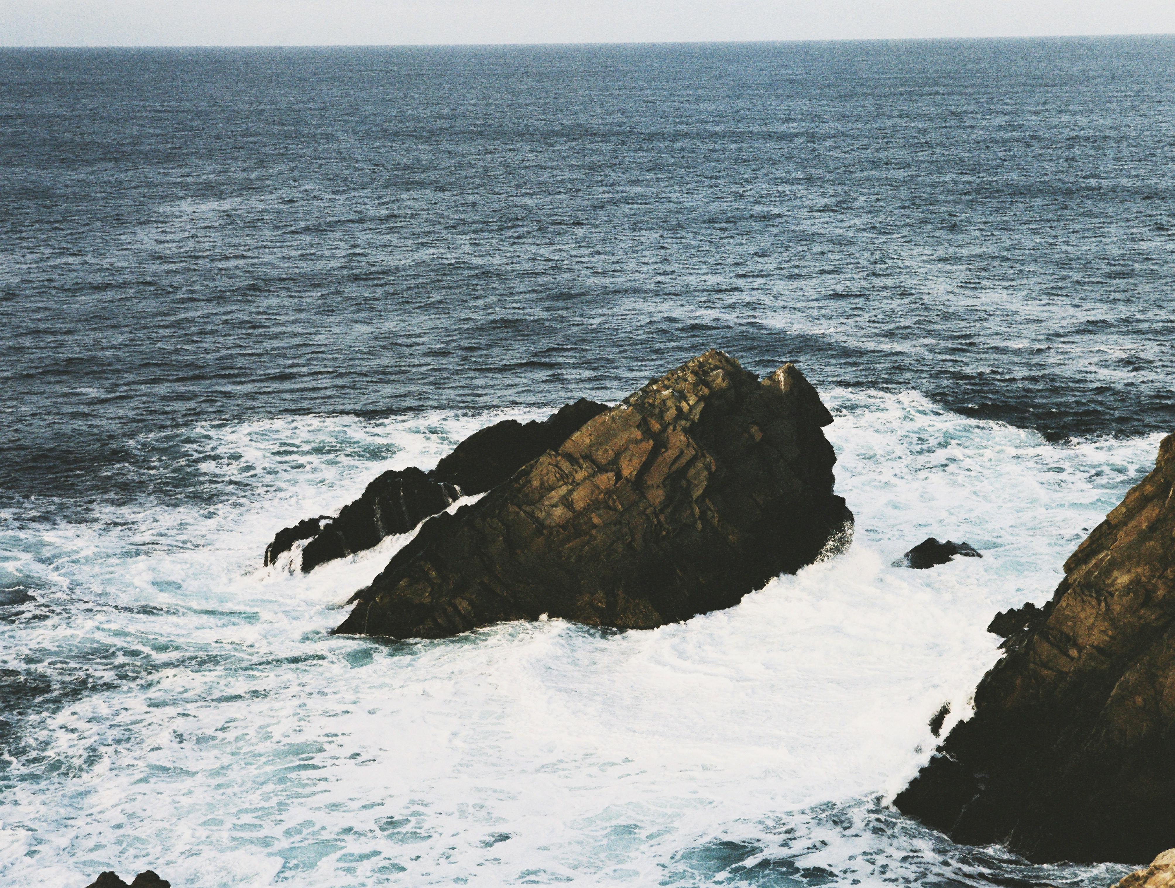 Taken on medium format CineStill film with a Mamiya 645. Waves crashing on rocks in the ocean in Newfoundland, Canada.