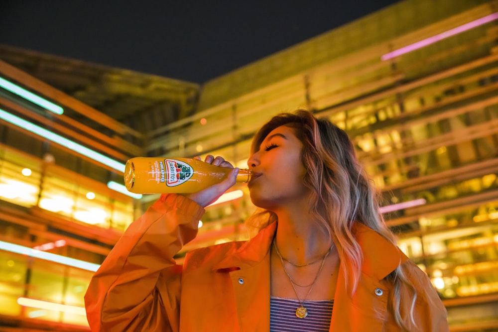 donna in blazer arancione che beve dalla bottiglia