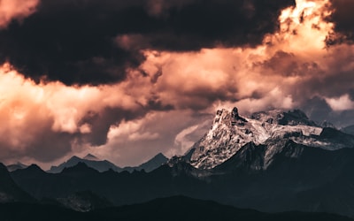 A wide shot of a rugged mountain range with dramatic clouds rolling overhead.