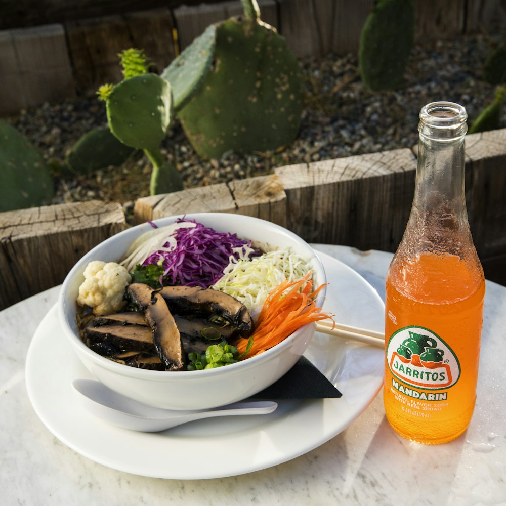 vegetable salad on white ceramic plate beside orange juice bottle