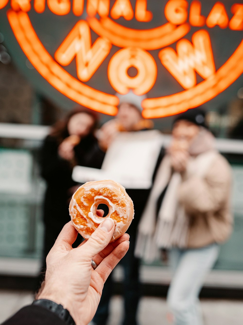 Person mit braunem Donut mit orangefarbenem und weißem Belag