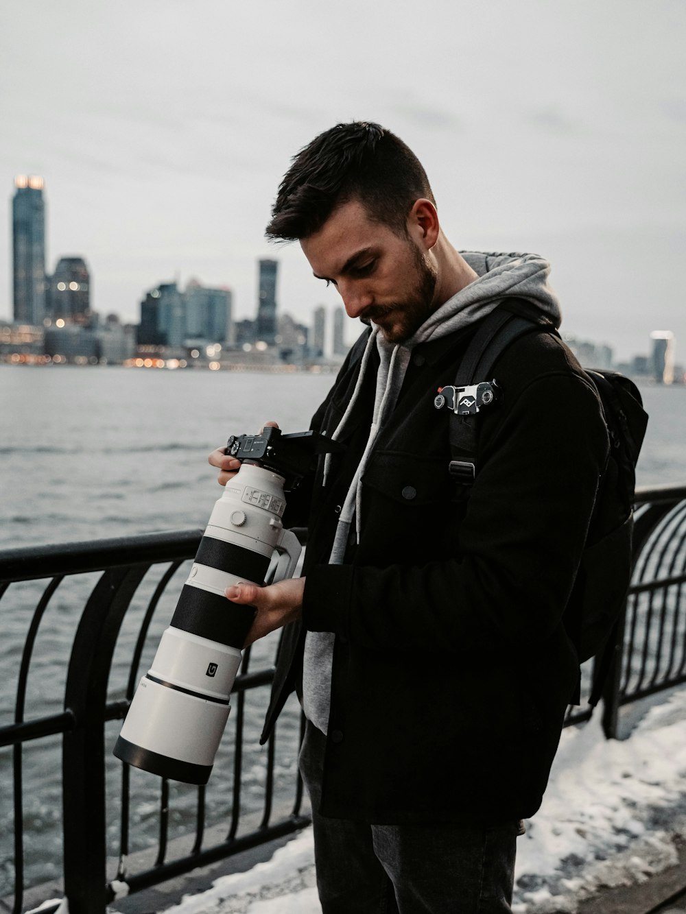 man in black jacket holding white and black dslr camera standing beside black metal railings during