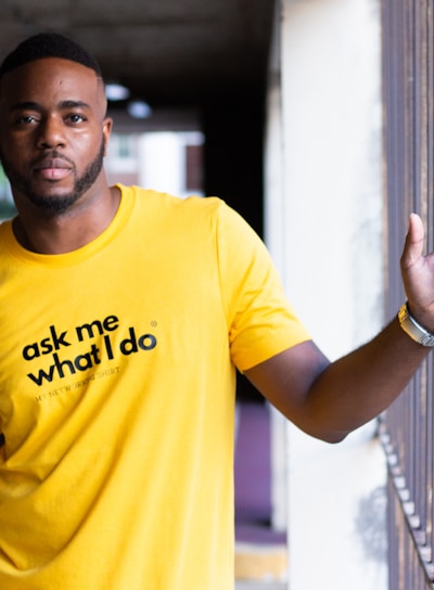 man in yellow crew neck t-shirt leaning on white wall