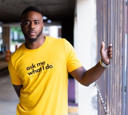 man in yellow crew neck t-shirt leaning on white wall