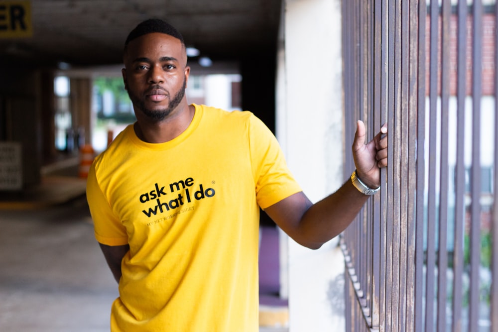 man in yellow crew neck t-shirt leaning on white wall