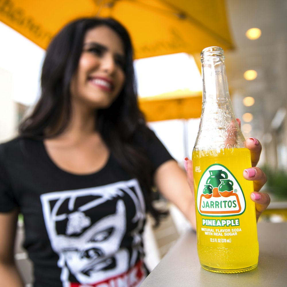 woman in black tank top holding orange juice bottle