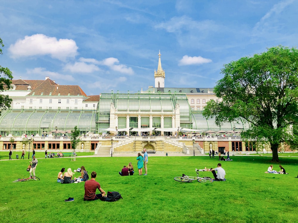 people sitting on green grass field near white concrete building during daytime