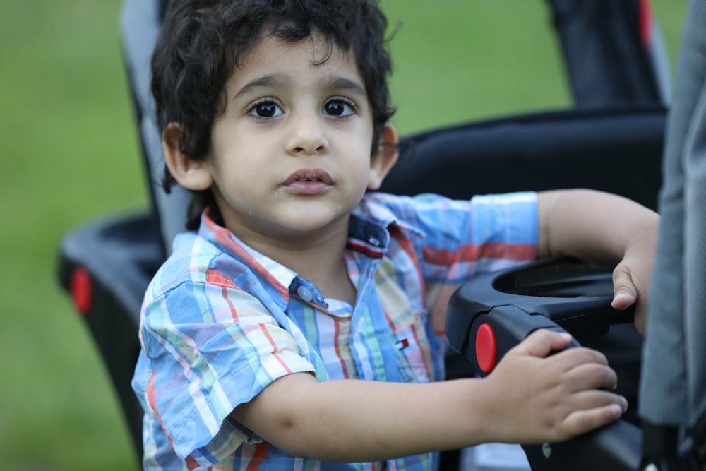 boy in blue white and red plaid button up shirt sitting on car seat