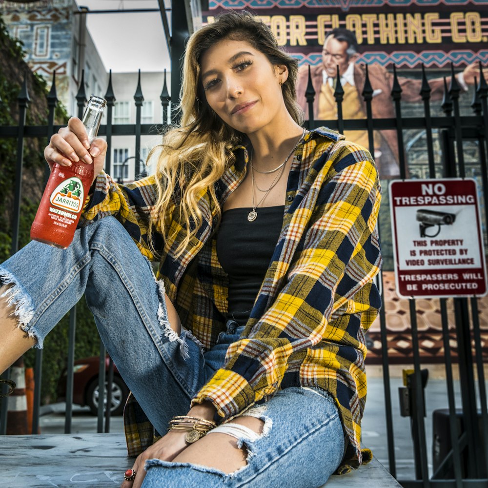 woman in yellow and black plaid shirt holding red and white labeled bottle