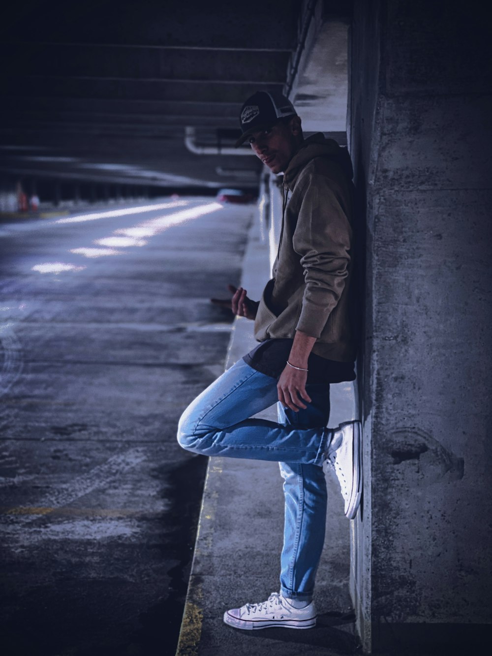 Hombre con chaqueta marrón y jeans de mezclilla azul sentado en una pared de concreto durante el día