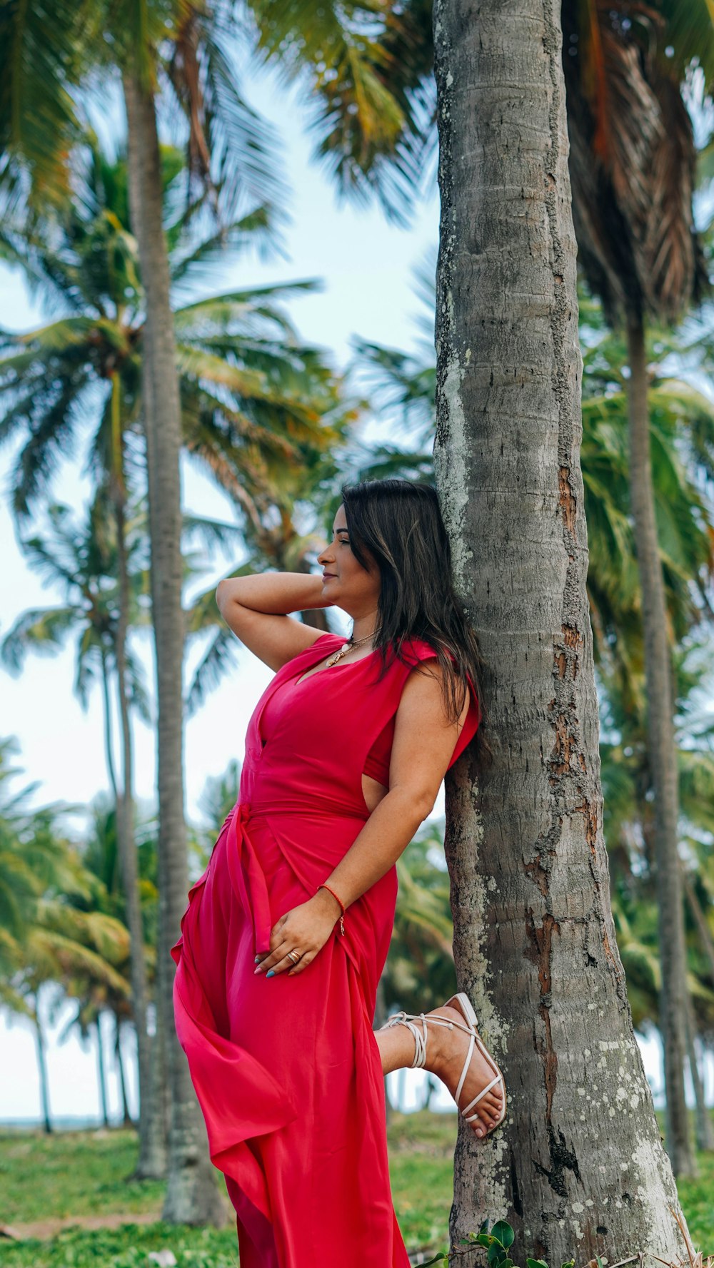 woman in red sleeveless dress leaning on brown tree during daytime