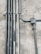 Multiple metal pipes are mounted along a textured concrete wall. The pipes vary in size and are arranged both vertically and horizontally, connected by clamps and a junction box.